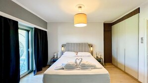 A modern hotel room with a large bed, a bedside table with a lamp, a wardrobe, and a window with curtains.