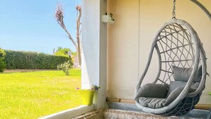 A patio with a hanging chair, a potted plant, and a view of a green field.