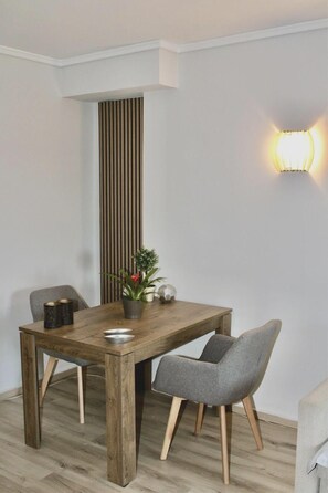 A dining area with a wooden table, two grey chairs, a potted plant, and a wall-mounted light fixture. - Beachside Retreat in Glyfada (Glifada)