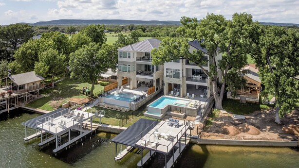 A modern house with a swimming pool, dock, and large trees.