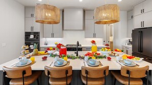 A modern kitchen with white cabinets, a central island with breakfast setup, and two hanging wicker light fixtures.