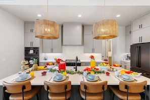 Una cocina moderna con armarios blancos, una isla central con espacio para desayunar y dos lámparas colgantes de mimbre.