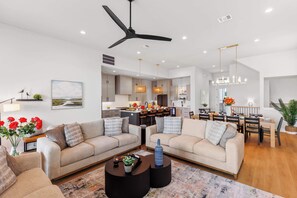 A modern living room with two sofas, a coffee table, and a dining area with a chandelier.