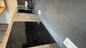 Una cocina con un fogón de inducción negro y dos tomas de corriente en la pared.