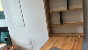 Una habitación con una mesa de madera, una mesita redonda pequeña con una lámpara, un sofá y un estante montado en la pared.