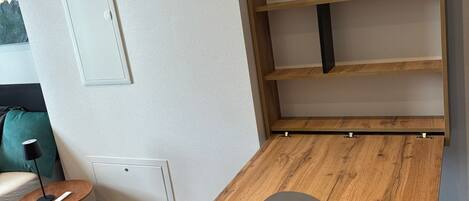 Une pièce comprenant une table en bois, une petite table d’appoint ronde avec une lampe, un canapé et une étagère fixée au mur.
