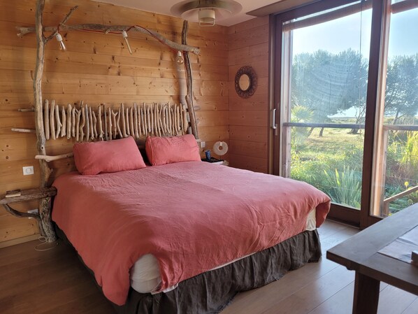 A wooden cabin bedroom with a bed, a nightstand, and a large window.