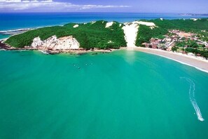 Une vue aérienne d’une zone côtière comprenant une plage, une petite ville et une colline boisée.