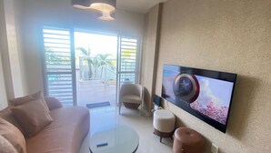 A modern living room with a sofa, a coffee table, and a TV mounted on the wall displaying a movie scene. - NYC Park Ave Beach Apt •3BR • Private Pool • Oceanview in Ponta Negra Natal (Ponta Negra Natal)