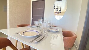 A dining table set with plates, cutlery, and glasses, surrounded by chairs. - NYC Park Ave Beach Apt •3BR • Private Pool • Oceanview in Ponta Negra Natal (Ponta Negra Natal)