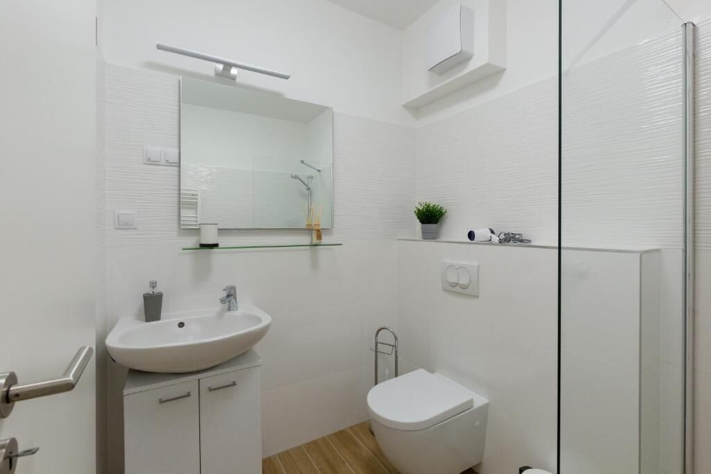A modern bathroom with a white sink, mirror, and toilet.