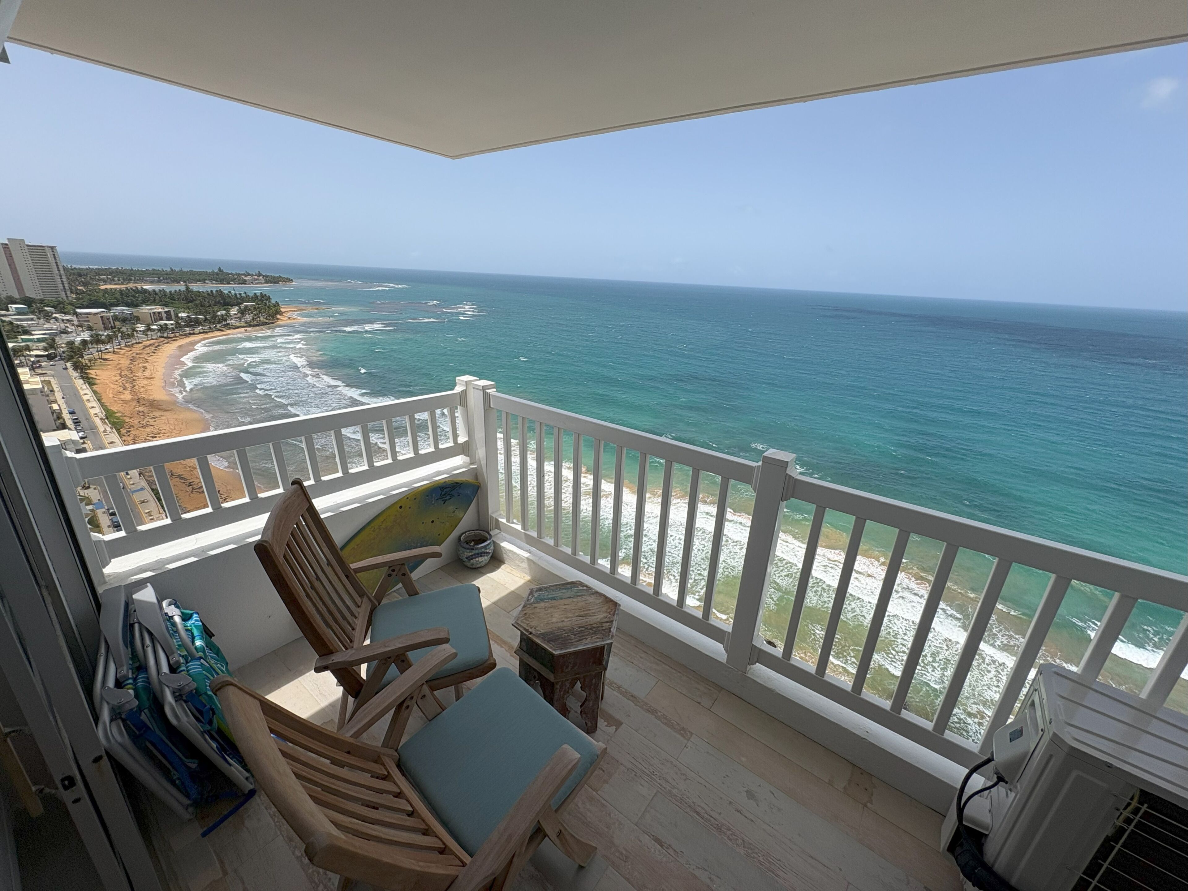 A balcony with a view of the ocean, wooden chairs, a small table, and a white railing.