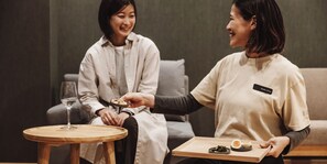 Two people seated on a couch with a small round table between them. One person is holding a tray with food and a glass. - BedandVegetable Kahoku (Kahoku)