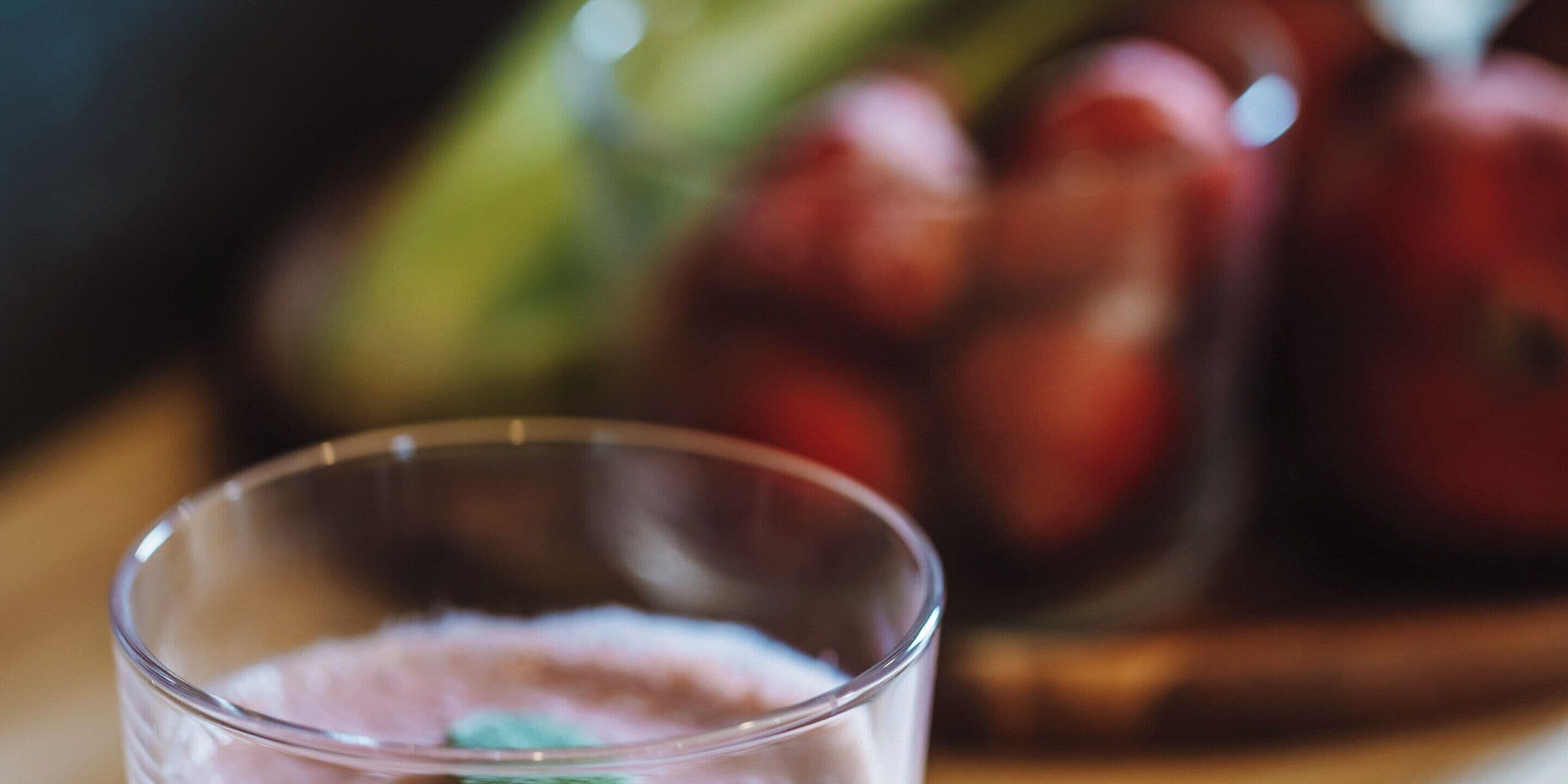 Un vaso transparente con un líquido rosado, posiblemente una bebida, en primer plano.