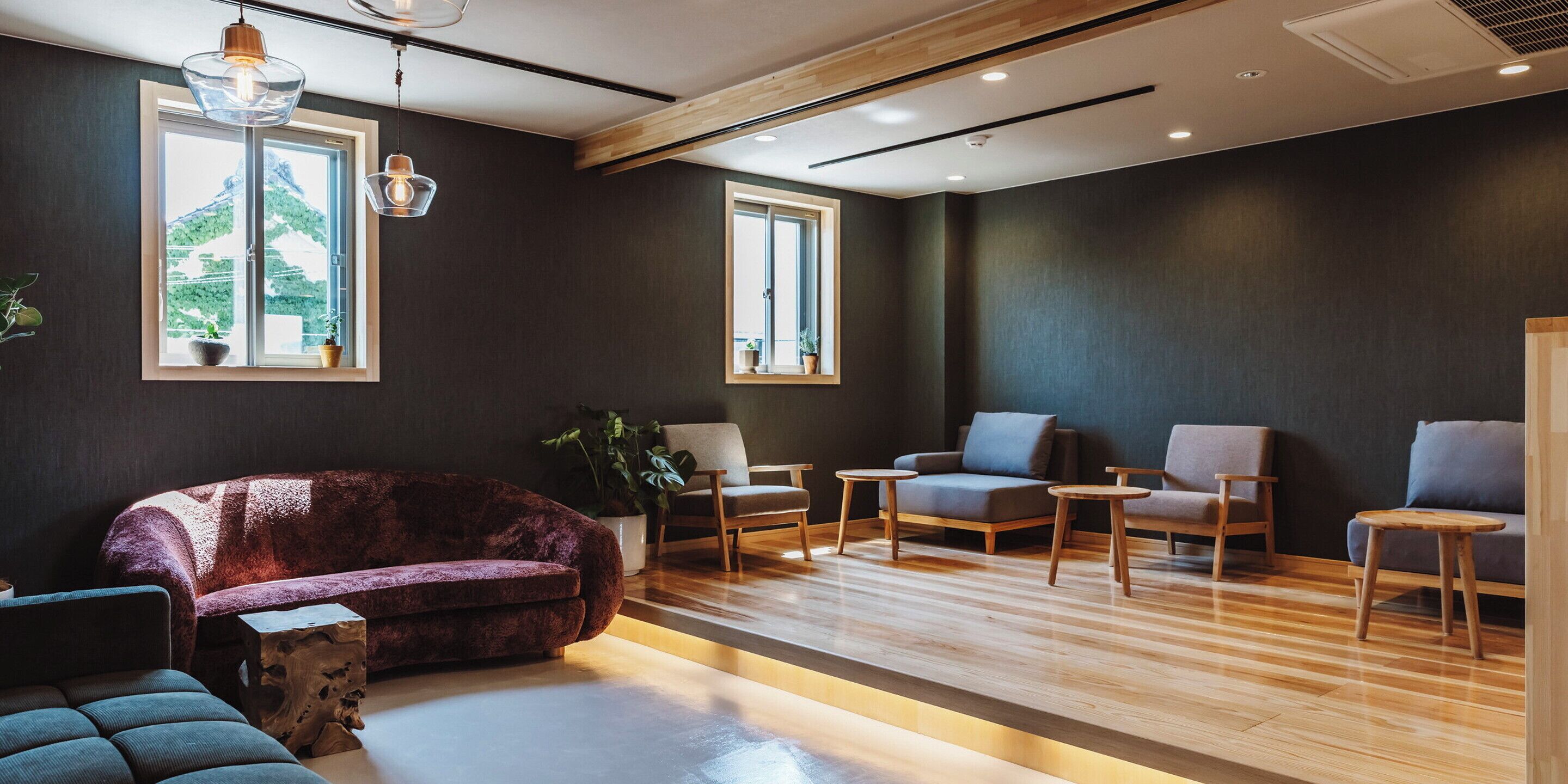 A modern interior with a dark wall, wooden flooring, and a seating area with a purple sofa and multiple chairs.