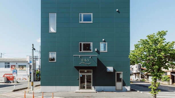 Un bâtiment moderne à la façade plate, doté de nombreuses fenêtres et d’une enseigne indiquant « B&V ».