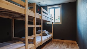 Une chambre avec des lits superposés, une fenêtre laissant entrer la lumière naturelle, un plancher en bois et un mur de couleur sombre.