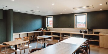 Interior moderno de restaurante com uma longa mesa comunitária, assentos individuais e área de cozinha visível através do balcão.