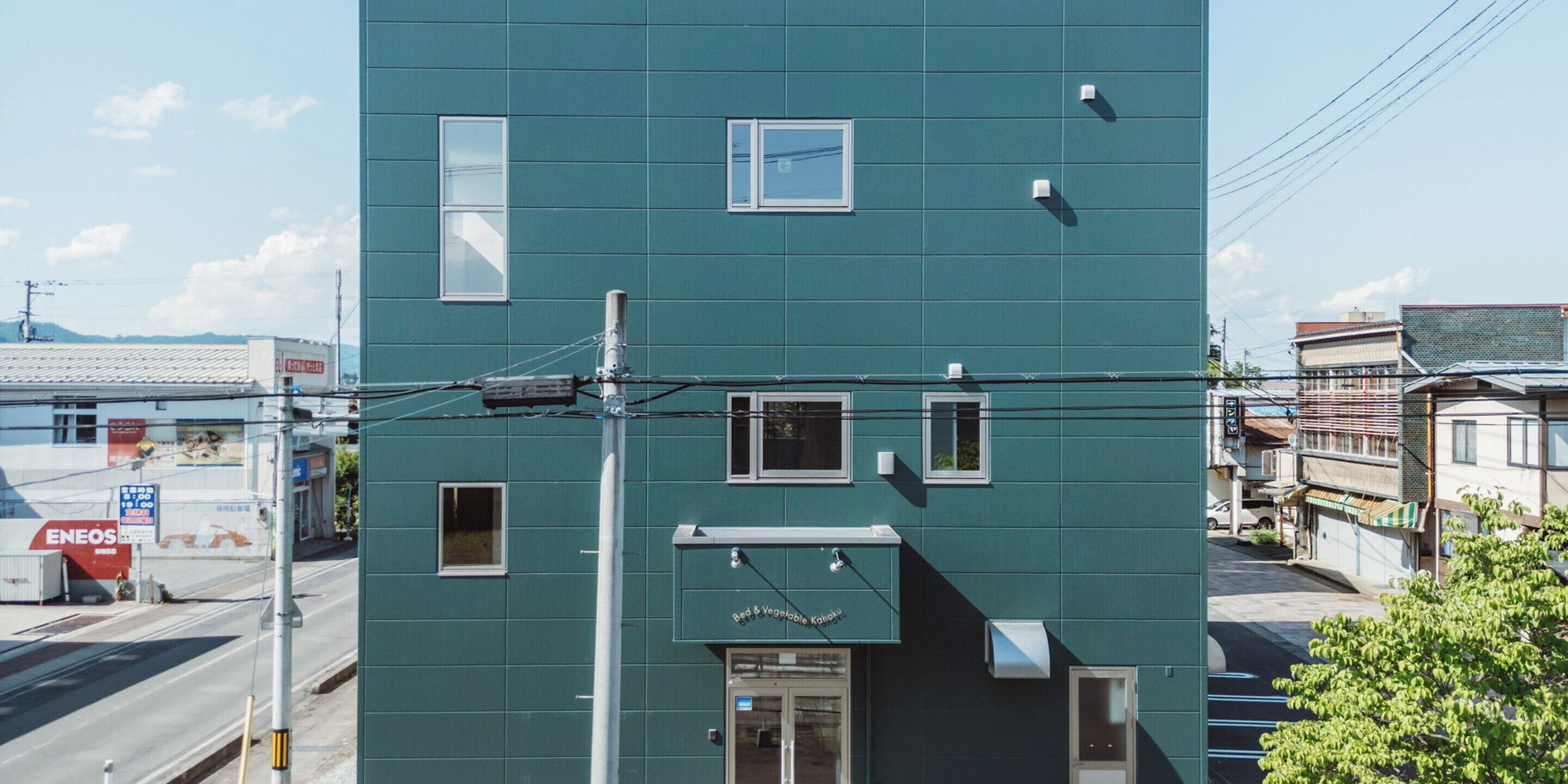Un edificio de varios pisos con fachada verde, varias ventanas y una entrada visible.