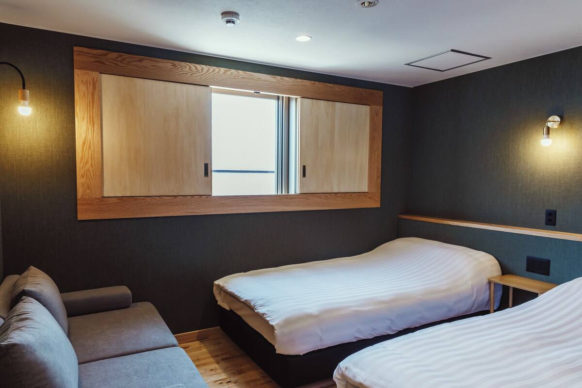 A room with two beds, a wooden ceiling panel, and wall-mounted lights.