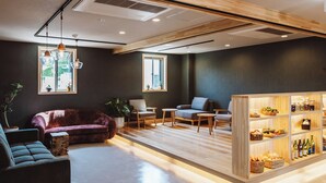 Un salon moderne comprenant un canapé, des fauteuils, une table basse et un meuble en bois contenant des bocaux et des bouteilles.