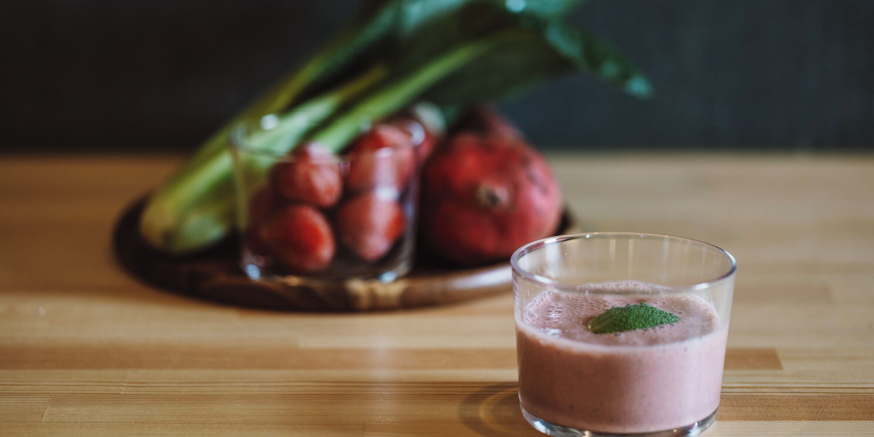 A glass of pink smoothie with a mint leaf on a wooden table.