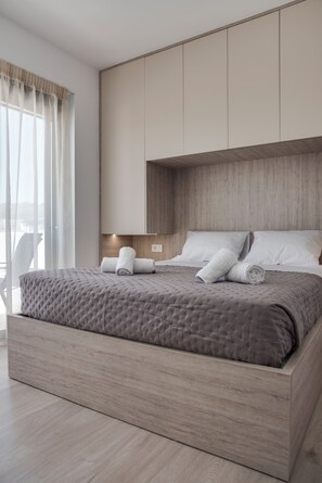 A modern bedroom with a large bed, wooden headboard, and a view of the city.