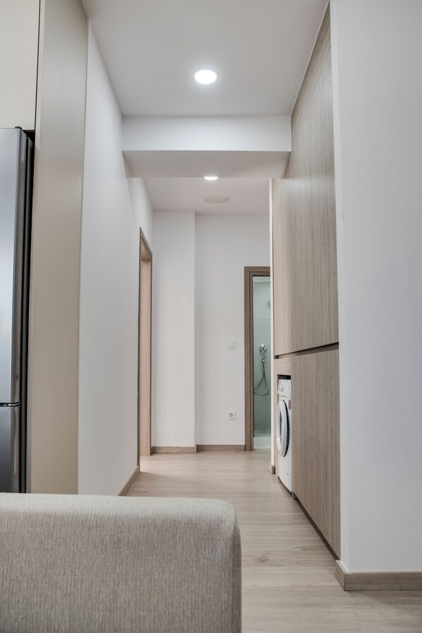 A narrow hallway with a washing machine, a refrigerator, and a sofa.