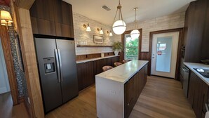 A modern kitchen with a built-in refrigerator, a marble countertop island, wooden cabinetry, and pendant lighting.