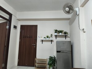A kitchen with a wooden door, a refrigerator, and shelves with potted plants.