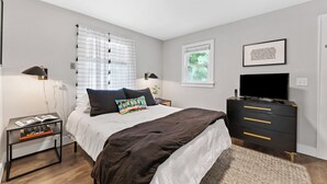 A modern bedroom with a bed, bedside tables, a dresser, a TV, and a window with blinds. - Optimist Abode 4: Chic Stay in the <3 of CLT with Greenway Access (Charlotte)