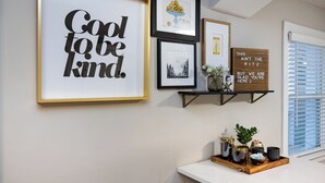 A wall with framed artwork, a shelf with decorative items, and a window with blinds. - Optimist Abode 4: Chic Stay in the <3 of CLT with Greenway Access (Charlotte)