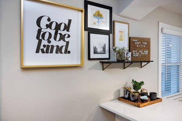 A wall with framed artwork, a shelf with decorative items, and a window with blinds.