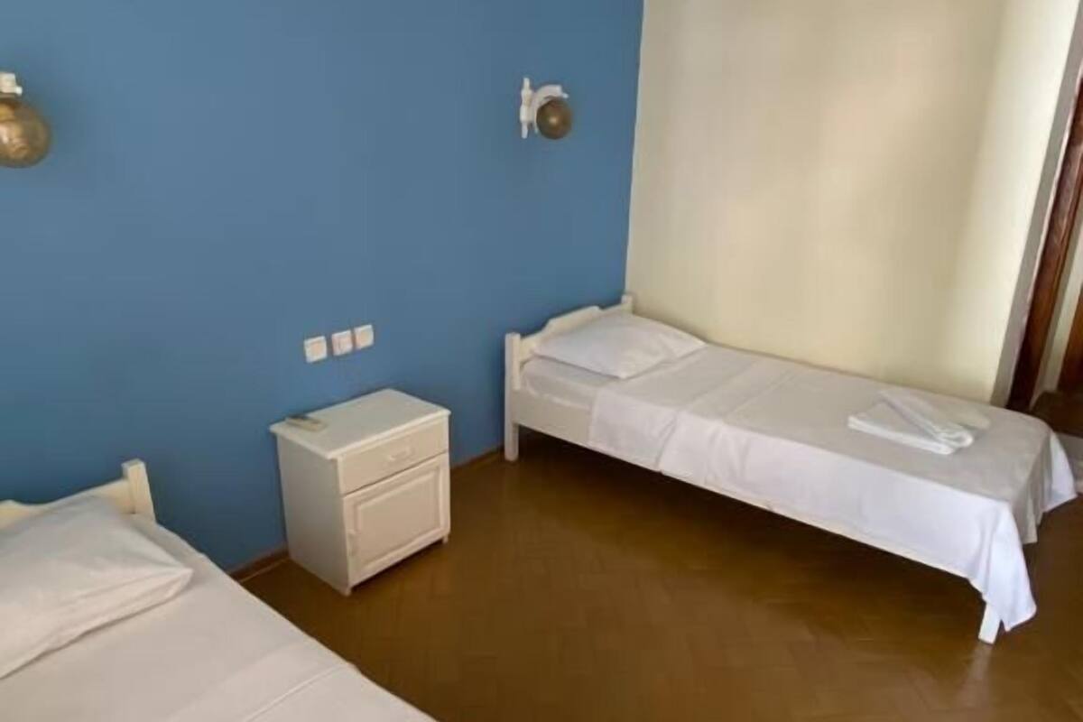 A hotel room with two beds, a small bedside table, a wall-mounted heater, and a window with curtains.