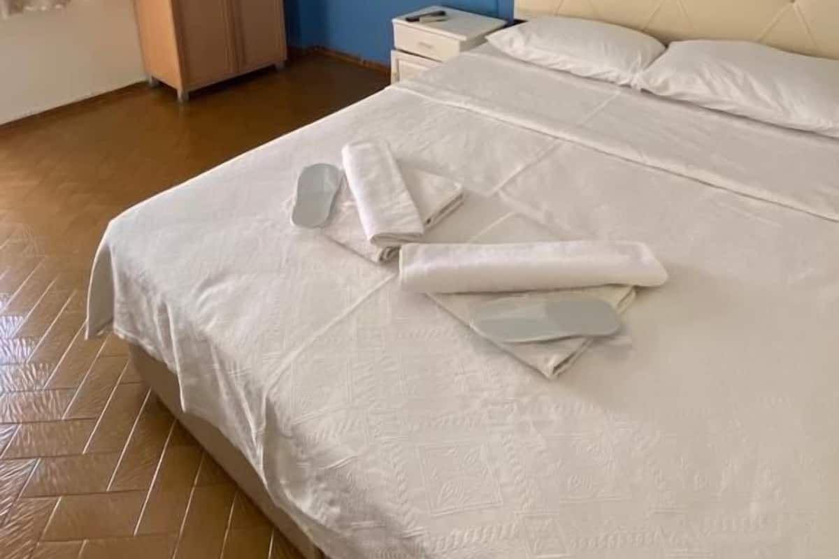 A hotel room with a large bed, a wardrobe, an air conditioning unit, and a nightstand.