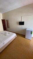 Una habitación de hotel con una cama, un televisor montado en la pared y un cesto de basura.