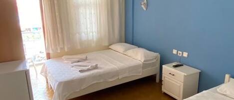 Habitación de hotel con dos camas, un escritorio, una silla, una ventana con cortinas y aire acondicionado instalado en la pared.