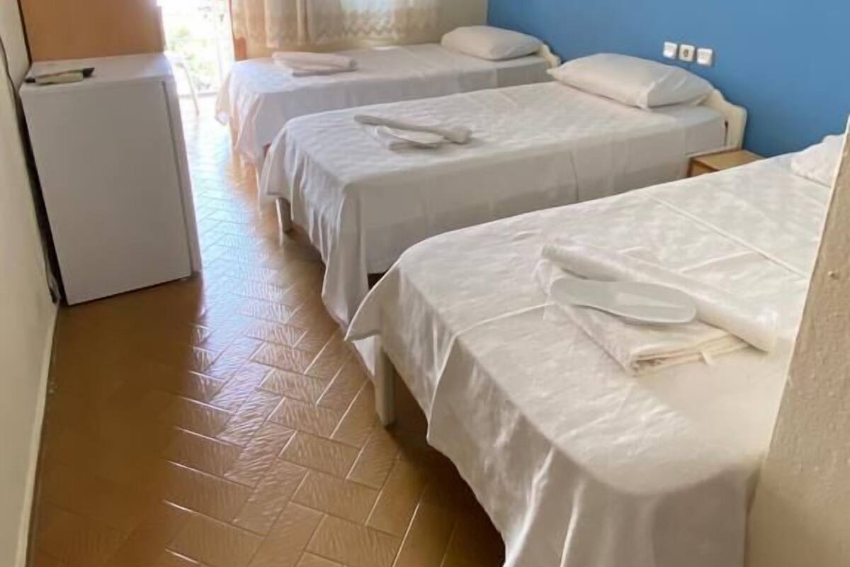 A hotel room with three single beds, a small refrigerator, and a window with curtains.