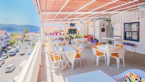 A balcony with outdoor seating, a TV, and a view of a street and buildings. - Saray Otel (Kas)