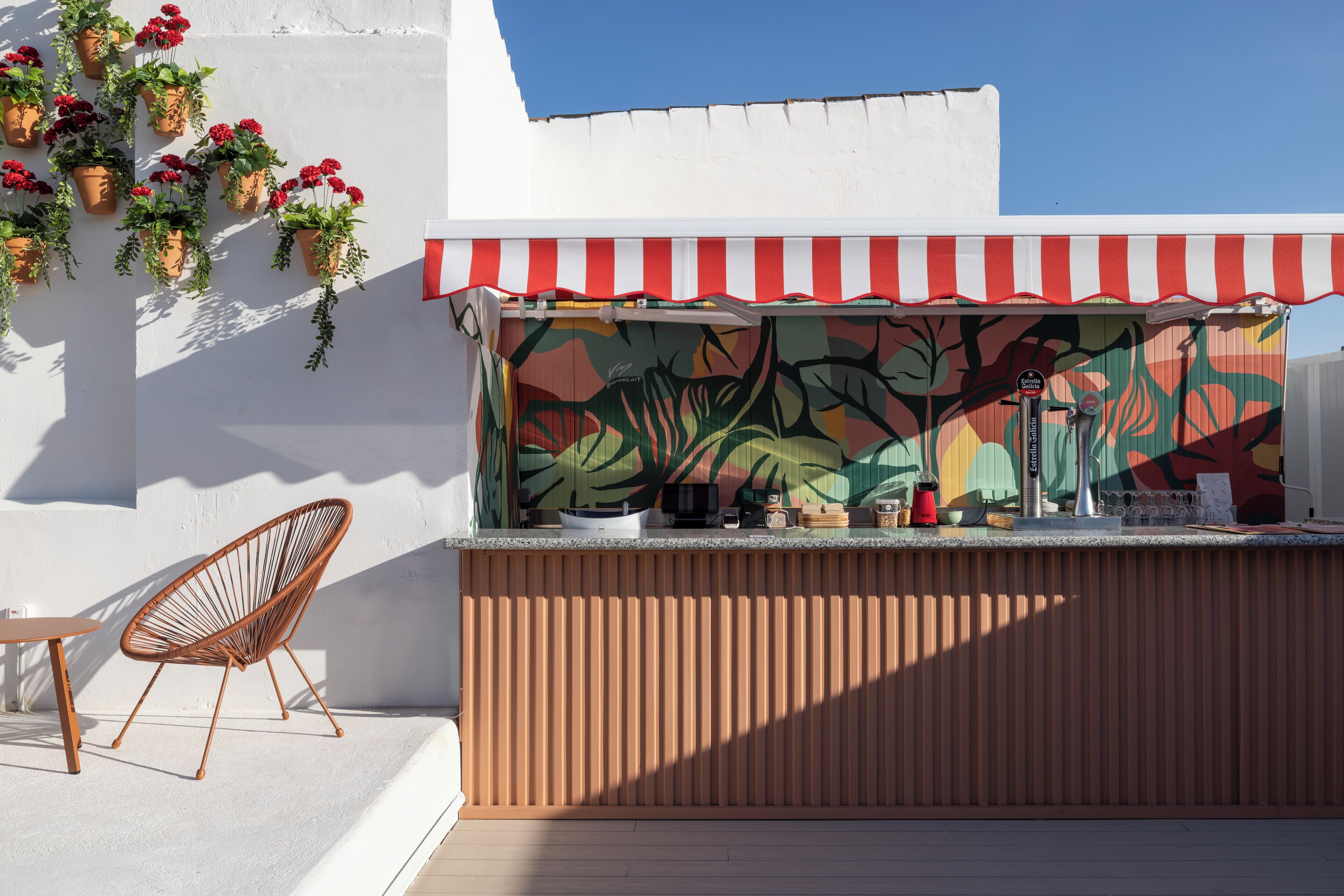 A bar area with a red and white striped awning, a wooden counter, and potted plants.
