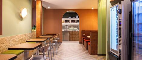 A modern restaurant with a long counter, chairs, and a refrigerator.