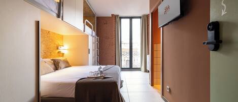 Une chambre d’hôtel de taille réduite, comprenant un lit, une table de chevet et un téléviseur fixé au mur.
