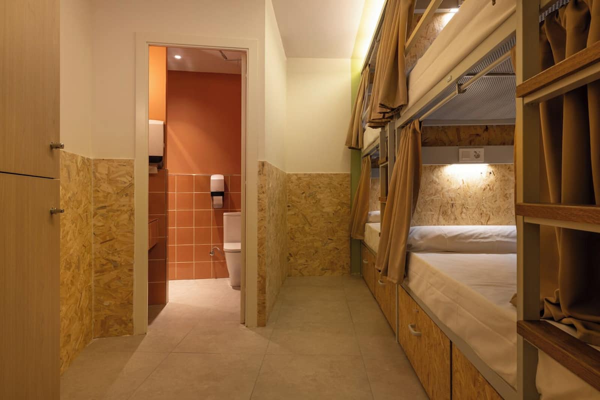 A compact room with bunk beds, a wooden wardrobe, a toilet, and a shower area.