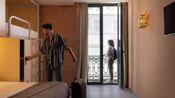 Une chambre d’hôtel avec un lit superposé, une valise et un balcon offrant une vue.