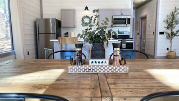 A dining area with a wooden table, metal chairs, a chessboard centerpiece, and a kitchen in the background.