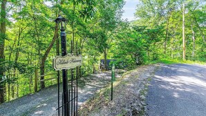 A signpost with 'Hillbould Lodge' written on it, surrounded by a forested area with a gravel path.