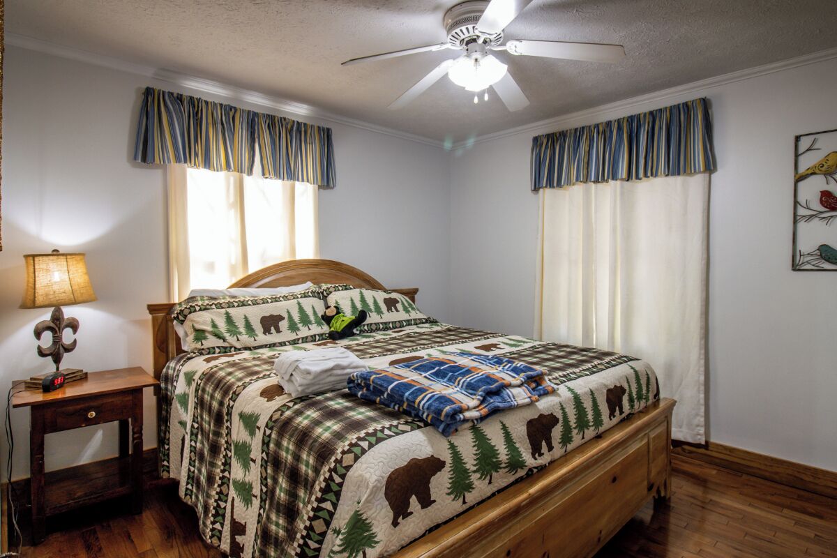 Un dormitorio con una cama de madera, una mesita de noche con una lámpara y un ventilador de techo.