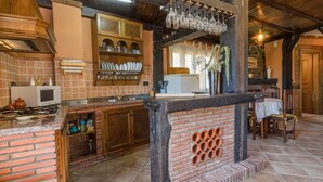 A kitchen with a brick backsplash, wooden cabinets, and a brick oven. There are wine glasses hanging above the counter and a table with chairs in the background. - Mulhacén Tourist Apartment (Lanjarón)