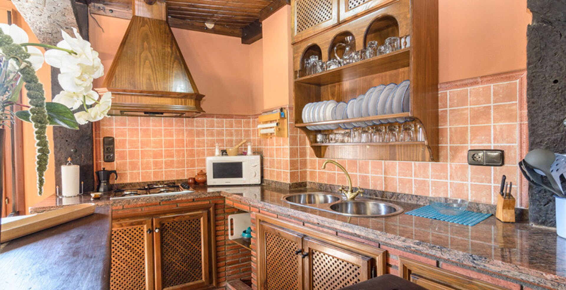 A kitchen with a wooden island, a sink, a microwave, and a hanging light fixture.