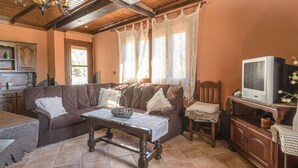 A cozy living room with a brown sofa, a wooden coffee table, a television, and a kitchen area with cabinets and a countertop. - Mulhacén Tourist Apartment (Lanjarón)